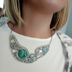 May include: A silver wire-wrapped necklace with a large, round turquoise stone and smaller turquoise and white stones. The necklace has an intricate, swirling design.