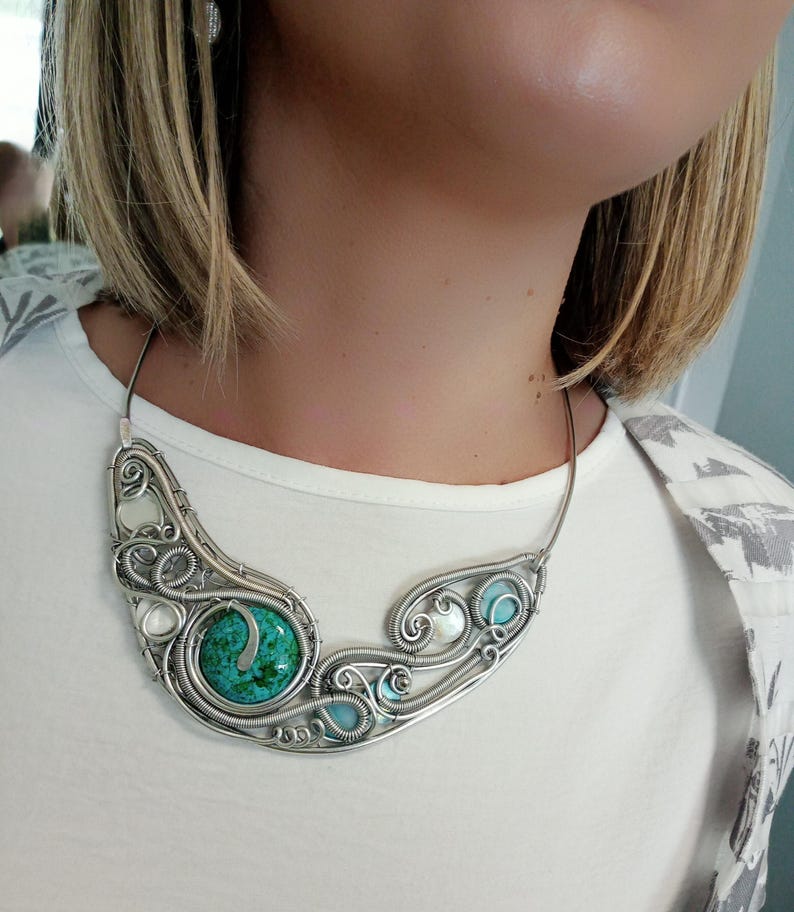 May include: A silver wire-wrapped necklace with a large, round turquoise stone and smaller turquoise and white stones. The necklace has an intricate, swirling design.