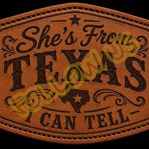 Op de afbeelding: Een rechthoekige bruine leren patch met afgeronde hoeken en gestikte randen. De tekst luidt She's From TEXAS I CAN TELL, met een ster boven de tekst en een silhouet van de staat Texas met een ster erin, alles in donkerbruin.