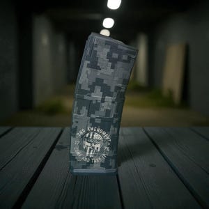 May include: A digital camouflage magazine with a skull graphic and the text "2ND AMENDMENT, COME AND TAKE IT". The magazine is primarily grey and black, with a rectangular shape and a curved design.