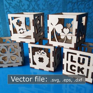 May include: Five wooden boxes with laser cut designs of shamrocks, a pot of gold, a leprechaun hat, and the word "LUCK". The boxes are stacked on a blue surface.