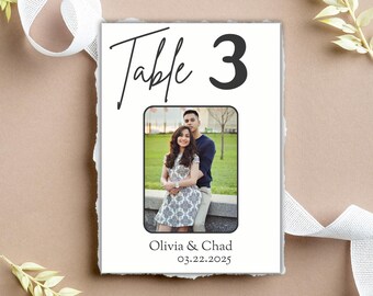 Puede incluir: Número de mesa 3 con una foto en blanco y negro de una pareja frente a un edificio. El texto "Table 3" está en negro con un contorno blanco. El texto "Olivia & Chad" y "03.22.2025" está en negro.