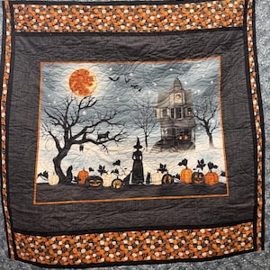 May include: A square quilt featuring a central panel with a Halloween scene of a witch, a haunted house, a full moon, and pumpkins. The border is made of black fabric with a small orange pumpkin print, and the quilting has a swirling pattern.