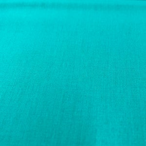 Puede incluir: Primer plano de una tela turquesa con una sutil textura tejida. La tela tiene un aspecto liso y un color uniforme. El material es probablemente un textil, posiblemente algodón o lino, adecuado para proyectos de ropa o decoración del hogar.