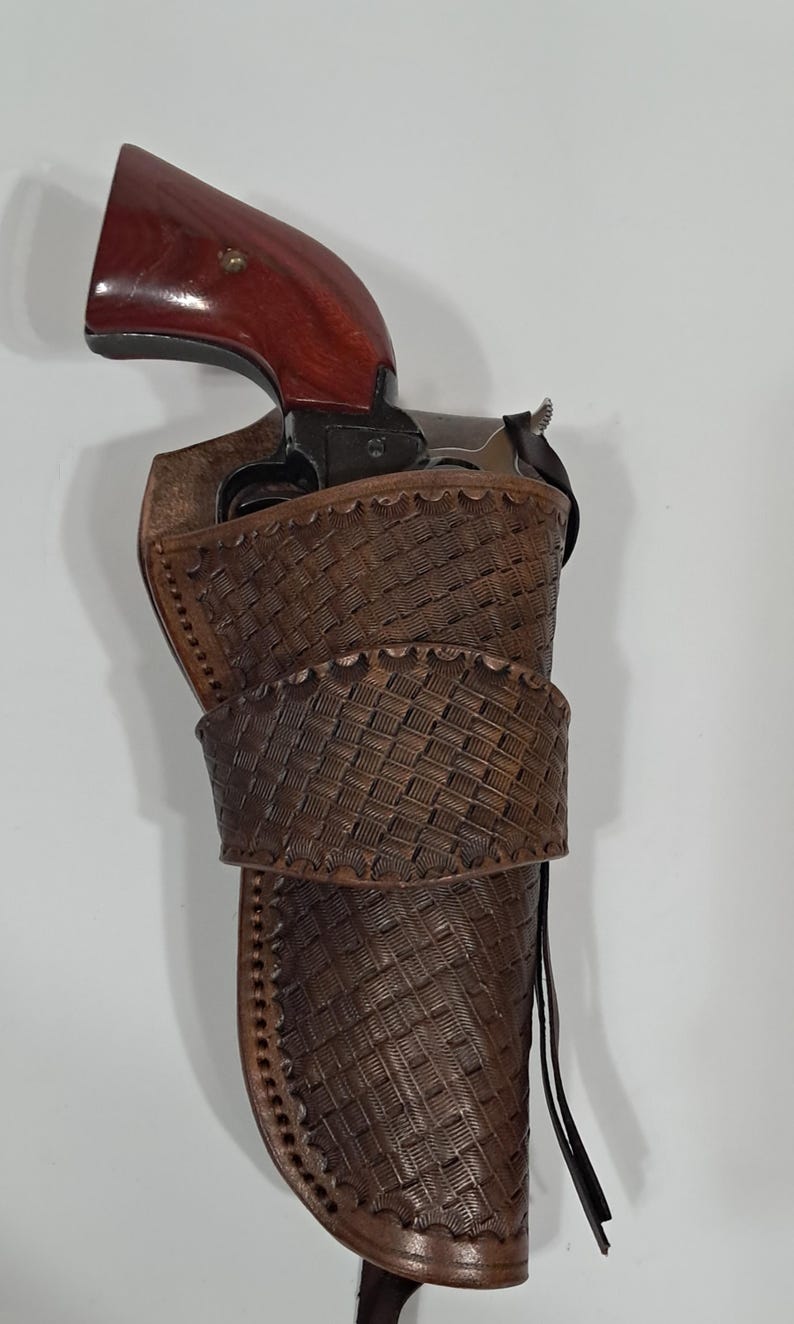May include: A brown leather holster with a woven design, holding a revolver with a dark wooden grip. The holster has a belt loop and a strap. The revolver is partially visible.