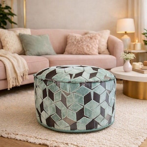 May include: A round, low-profile ottoman featuring a textured fabric surface with a repeating geometric cube pattern in shades of light mint green and dark charcoal gray. The cylindrical piece has a flat top and a structured, piped edge design.