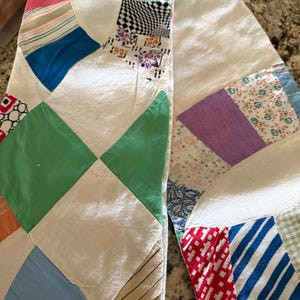 May include: Close-up of a handmade quilt with a variety of colorful fabric patches. The quilt features a white background with curved and diamond-shaped sections. The patches include stripes, floral patterns, and solid colors like green, blue, and red.