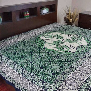 May include: A green and white tapestry featuring a Celtic knot design with a circular pattern in the centre. The tapestry is on a bed with a dark brown headboard.