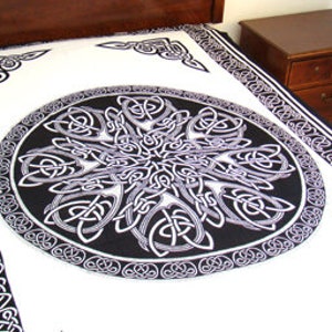 May include: A white tapestry with a black and white Celtic knot design. The design features a large circular knot in the center and smaller knots around the border.