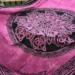 May include: A pink tapestry with a black and pink Celtic knot design. The design is a circle with a large knot in the center and smaller knots around the edge.