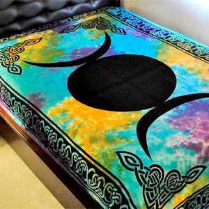 May include: A tapestry with a tie-dye pattern in shades of blue, yellow, purple, and green. The tapestry features a black triple moon symbol with a Celtic knot border.