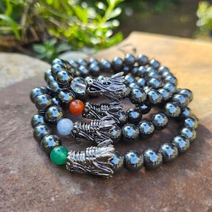 May include: Three black hematite beaded bracelets with silver dragon head charms. Each bracelet has a different colored gemstone bead: clear, orange, blue, and green.