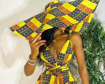 May include: A yellow, blue, and orange patterned jumpsuit with a matching wide-brimmed sun hat. The jumpsuit has a V-neck and a wrap-style waist.