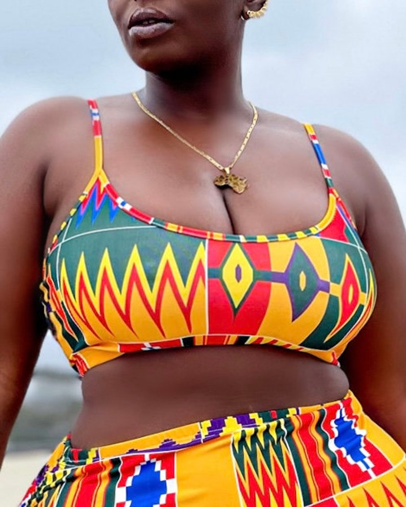 Op de afbeelding: Een tweedelig badpak met een kleurrijk Afrikaans printpatroon. De top is halter-stijl met een dunne band en de onderkant is een hoge taille bikini broek. Het badpak is gemaakt van een zachte, rekbare stof en is perfect voor een dag op het strand of bij het zwembad.