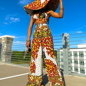 May include: A wide-brimmed hat with a white, red, and yellow floral pattern. The hat is paired with a matching crop top and wide-leg pants. The outfit is a vibrant and stylish choice for a summer day.