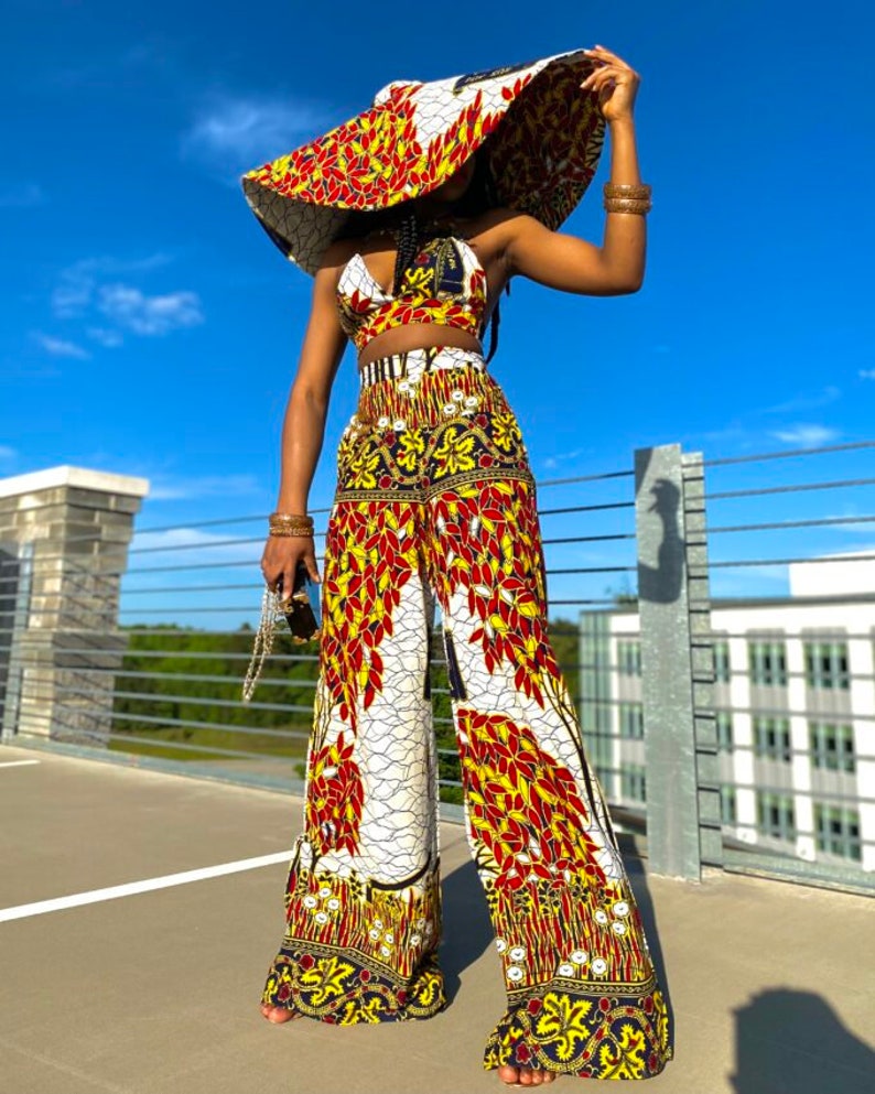 May include: A wide-brimmed hat with a white, red, and yellow floral pattern. The hat is paired with a matching crop top and wide-leg pants. The outfit is a vibrant and stylish choice for a summer day.