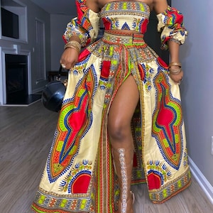 May include: A vibrant, off-the-shoulder two-piece dress with a high slit. The ensemble features a cream-colored base with a colorful pattern of red, green, blue, and yellow geometric shapes. The sleeves are puffed, and the skirt has a high slit, showcasing a clear sandal.