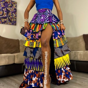 May include: A multi-layered skirt with a high slit, featuring a vibrant mix of colorful African print fabrics. The skirt is paired with a blue sleeveless top and clear heeled sandals.