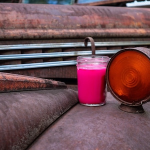 May include: A pink candle in a glass jar sits on a rusty truck bed next to an orange round light.