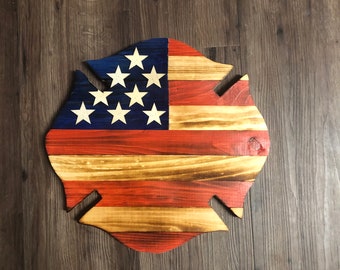 May include: A wooden American flag in the shape of a firefighter's Maltese cross. The flag is painted in red, white, and blue with a distressed finish.