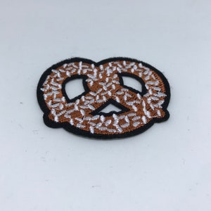 May include: A brown and white embroidered pretzel patch with a black border.