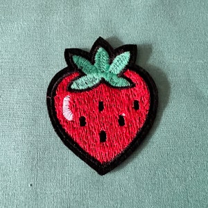 May include: An embroidered strawberry patch with red stitching, green leaves and black outlining.