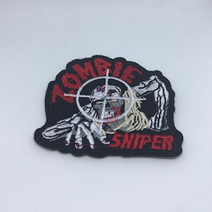 May include: Black embroidered patch featuring a white zombie in a red target with the words "Zombie Sniper" in red.