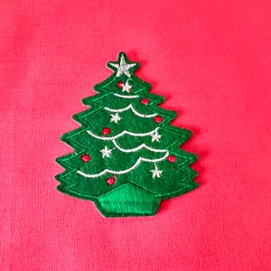 May include: A green felt Christmas tree applique with white stars and red baubles. The tree is on a red background.