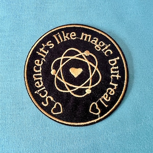May include: A black and gold embroidered patch with an atom symbol and the text "Science it's like magic but real".