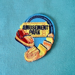 May include: A blue and yellow embroidered patch with the words "Amusement Park" and a cartoon roller coaster car.