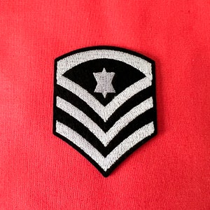 May include: A black and white embroidered patch with three white stripes and a white six-pointed star in the centre.