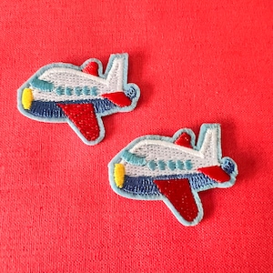 May include: Two blue and red embroidered airplane patches. The airplanes are white with blue and red details.