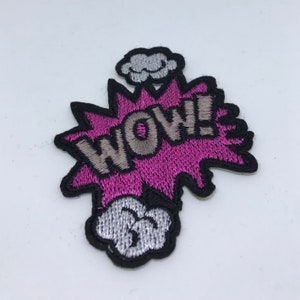 Op de afbeelding: Roze en grijze geborduurde patch met het woord "WOW!" in een spreekballon in stripboek stijl. De patch heeft een zwarte omtrek en een witte wolk boven de spreekballon.