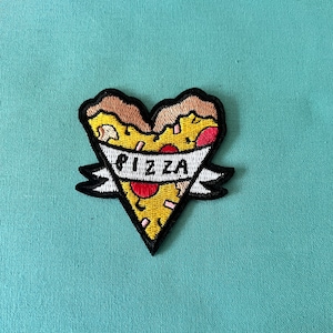May include: An embroidered patch shaped like a heart, featuring a pizza slice inside. The pizza has red pepperoni, white cheese, and a yellow crust. A white banner with the word "PIZZA" is wrapped around the pizza slice.