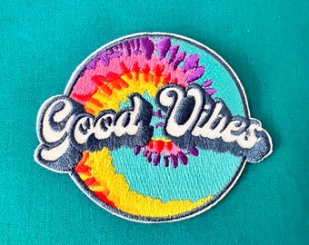May include: Embroidered patch with a tie-dye design in shades of yellow, orange, pink, purple, and blue. The words "Good Vibes" are embroidered in black with white outlines.
