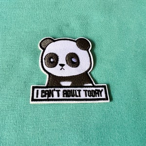 May include: Black and white embroidered iron-on patch featuring a cartoon panda with the text "I can't adult today".