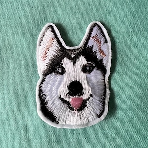 May include: Embroidered patch of a husky dog's face with white fur, black markings, and a pink tongue. The patch is white with a white outline.