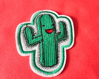 May include: Green embroidered cactus patch with a smiling face and raised arms. The patch is outlined in white and black thread.