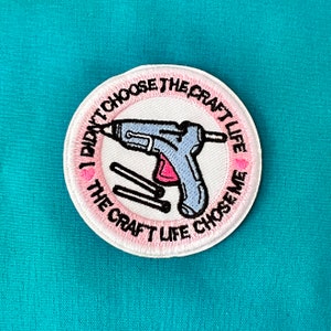 May include: White round patch with pink stitching. The patch features a cartoon image of a glue gun with a pink heart and the text "I didn't choose the craft life, the craft life chose me."