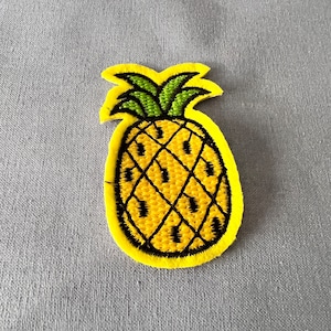Op de afbeelding: Een gele geborduurde ananas-patch met een groene bovenkant en zwarte stiksels.