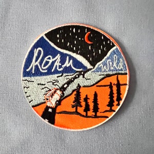 May include: Embroidered patch with a blue and orange landscape, a crescent moon, and the text "Roam Wild".