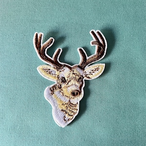 May include: A white and brown embroidered iron-on patch of a deer head with antlers.