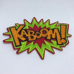 Könnte beinhalten: Ein gestickter Aufnäher in Rot und Grün mit dem Wort "KABOOM!" in orangefarbenen Buchstaben mit schwarzen Umrandungen.