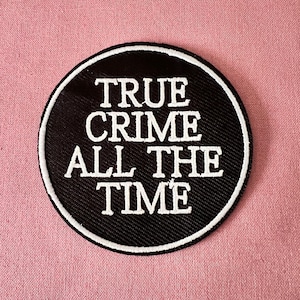 Könnte beinhalten: Runder schwarzer und weißer Patch mit dem Text "TRUE CRIME ALL THE TIME" in weißer Stickerei.