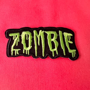 Peut inclure: Un patch brodé noir et vert avec le mot "ZOMBIE" en lettres vertes qui coulent.