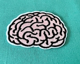 May include: A pink and black embroidered brain patch. The brain is outlined in black and has a detailed design.