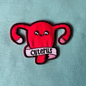 May include: Red felt patch with a cartoon uterus with a smiling face and the text "uterus" in a pink banner.