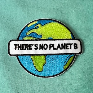 Może przedstawiać: Naszywka haftowana z niebieską i zieloną kulą ziemską i białym banerem z napisem "THERE'S NO PLANET B".