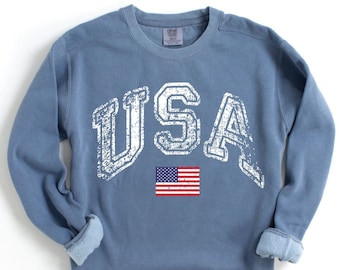 May include: A blue sweatshirt with a distressed white graphic of "USA" and a small American flag.