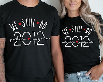 May include: A couple wearing black t-shirts with the text "WE STILL DO peter nicole 2012" and red hearts. The shirts are a matching set for a wedding anniversary.